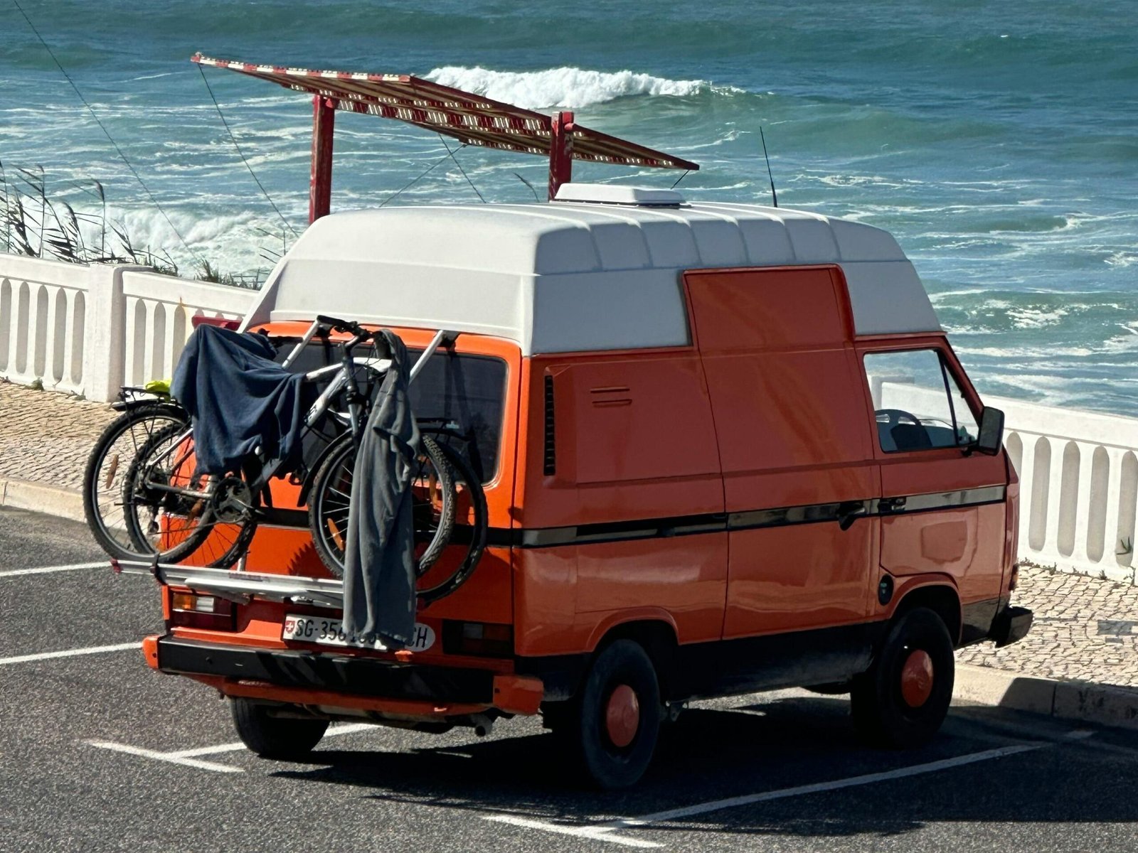 A classic orange van parked by the ocean with bicycles attached, offering a sense of adventure and exploration.